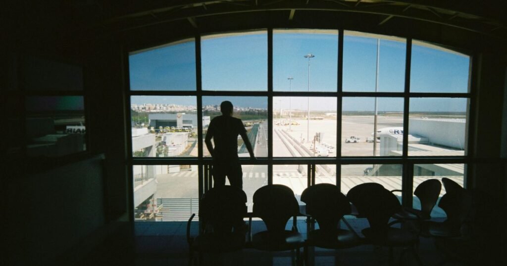 A silhouette of a person standing in an airport terminal, looking out large windows at planes on the tarmac. This image suggests a stop on a journey from Phoenix to Sequoia National Park, possibly involving a flight.